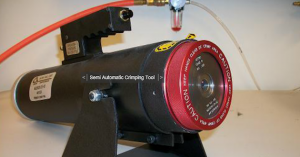 Close-up of a semi-automatic crimping tool with a red caution label.