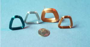 Four metallic trapezoidal rings in different colors next to a coin for scale.
